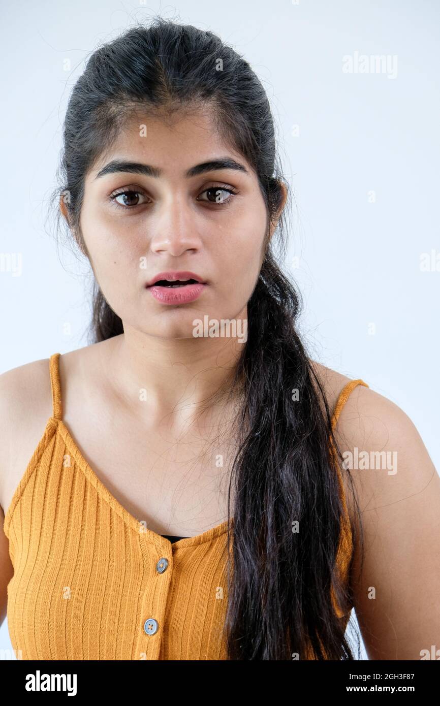 Surprised Indian girl in a yellow t shirt standing against a white wall Stock Photo Alamy