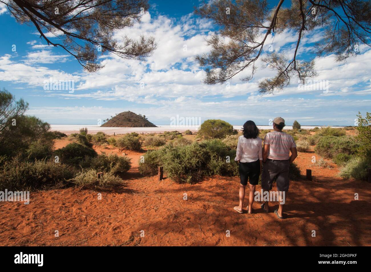 A male and female tourist viewing Lake Ballard in Western Australia, framed by the tree cover of the camp area overlooking the large salt lake. Stock Photo