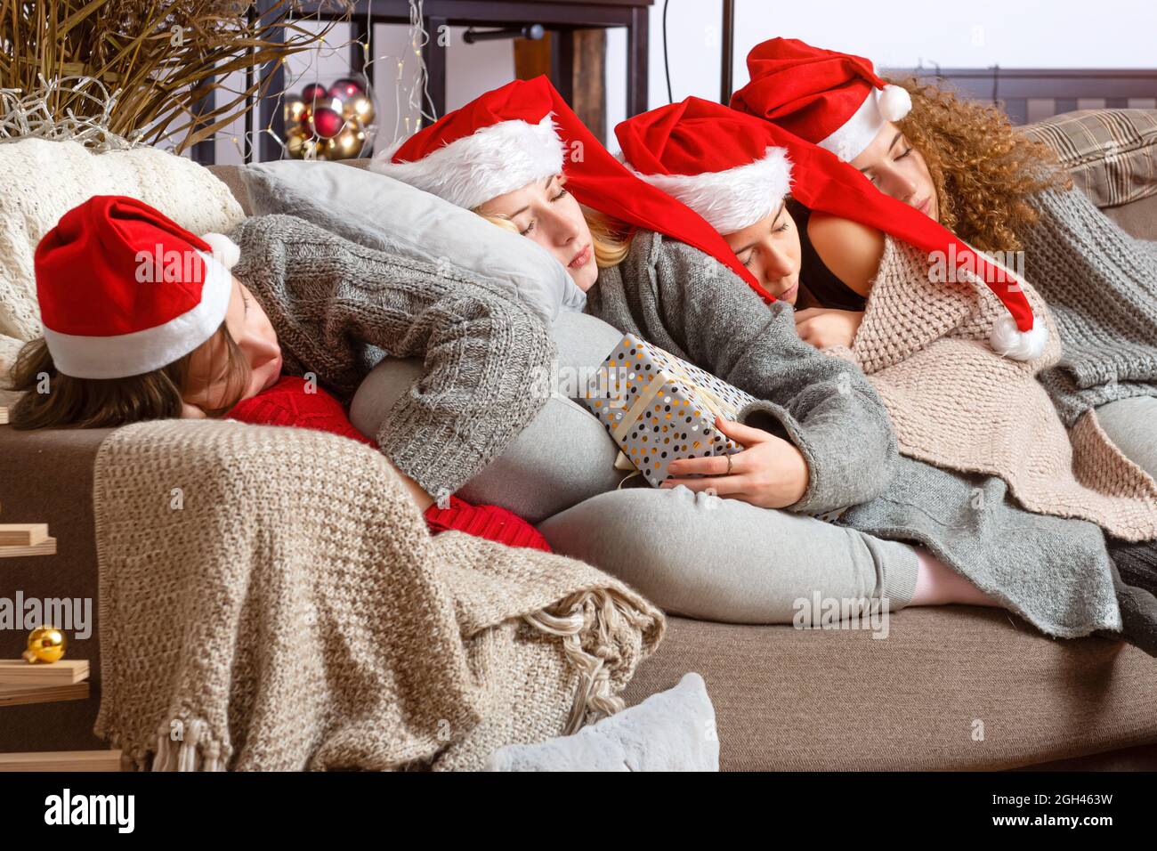 four young teen girls in red santa hats fell asleep on the couch after wrapping Christmas presents Stock Photo