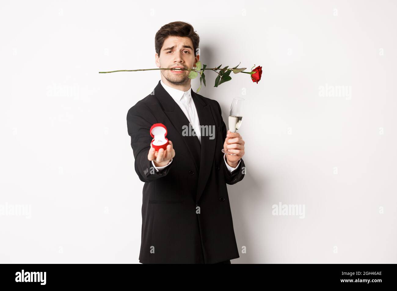 Romantic young man in suit making a proposal, holding rose in teeth and  glass of champagne, showing engagement ring, asking to marry him, standing  aga Stock Photo - Alamy