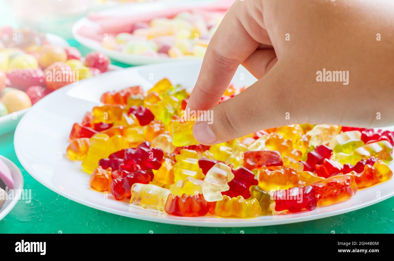 Hand takes colorful gummy bears candies of the plate. Close-up. Jelly treats for children and adults. Stock Photo