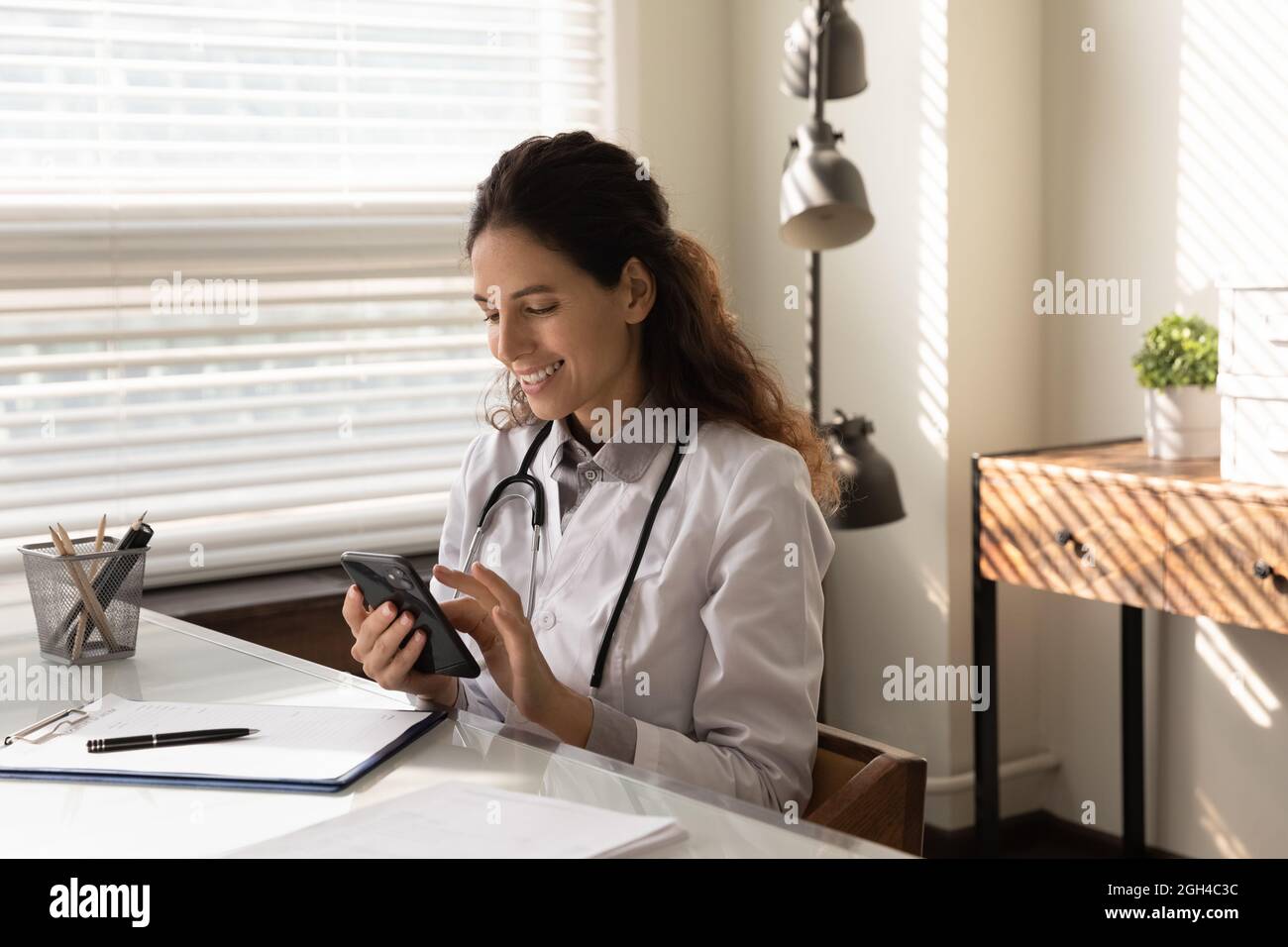 Happy young general practitioner chatting online on mobile phone Stock Photo