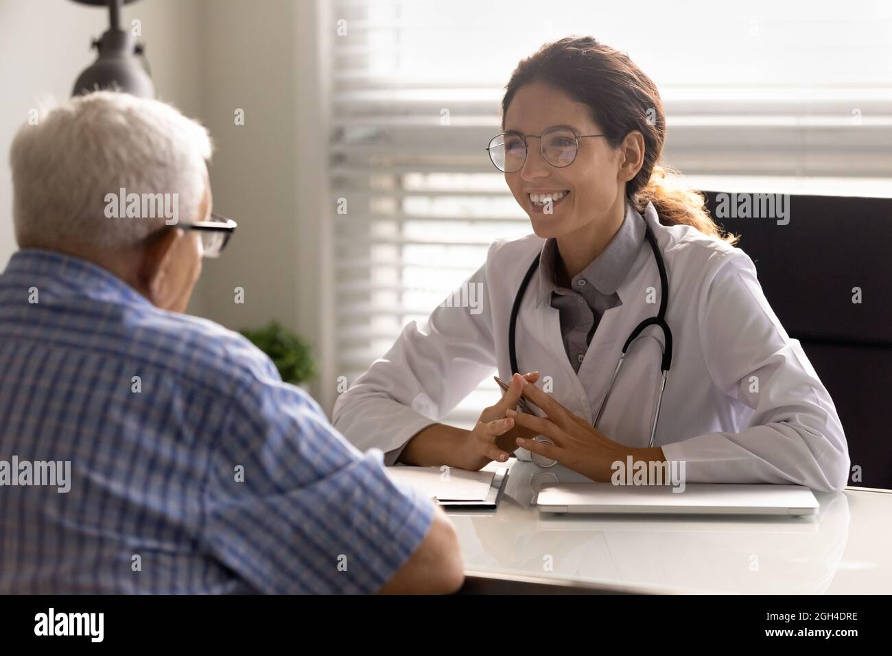 Happy young doctor and senior patient talking in hospital Stock Photo ...