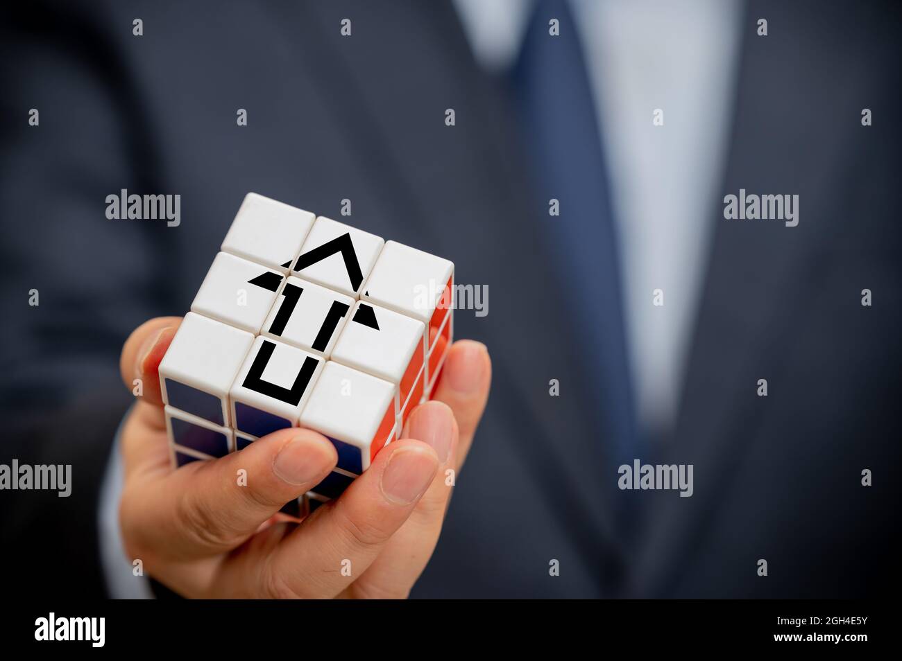 Hands of a businessman holding a cube with an arrow icon visible. Stock Photo