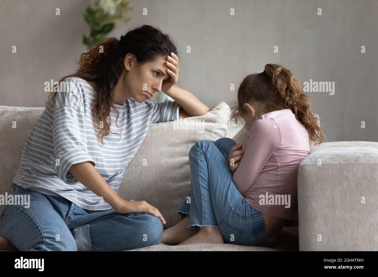 Young latin mother feeling guilty looking at stressed little kid. Stock Photo