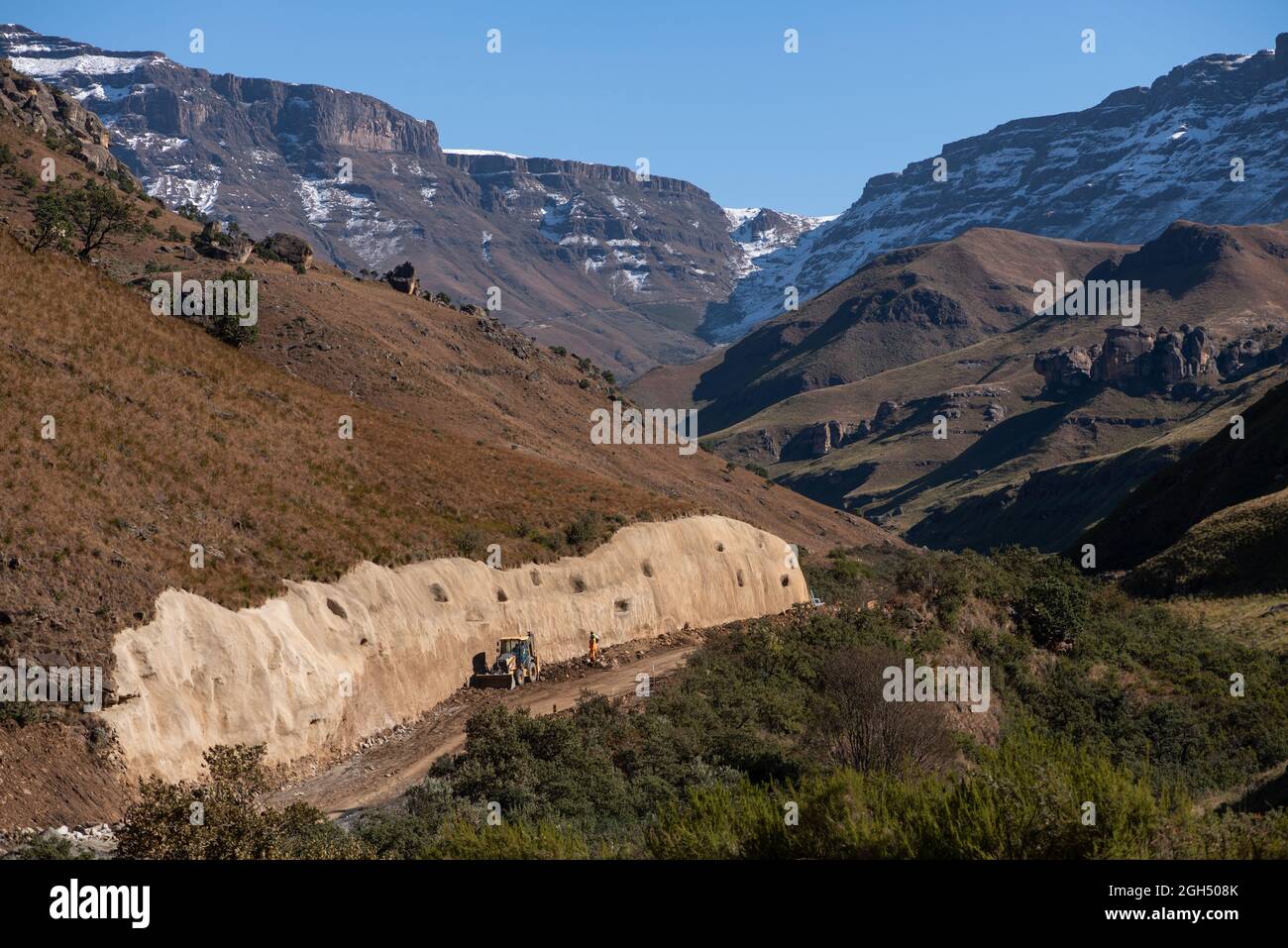 Road works along the Sani Pass with snow capped mountains in the background Stock Photo