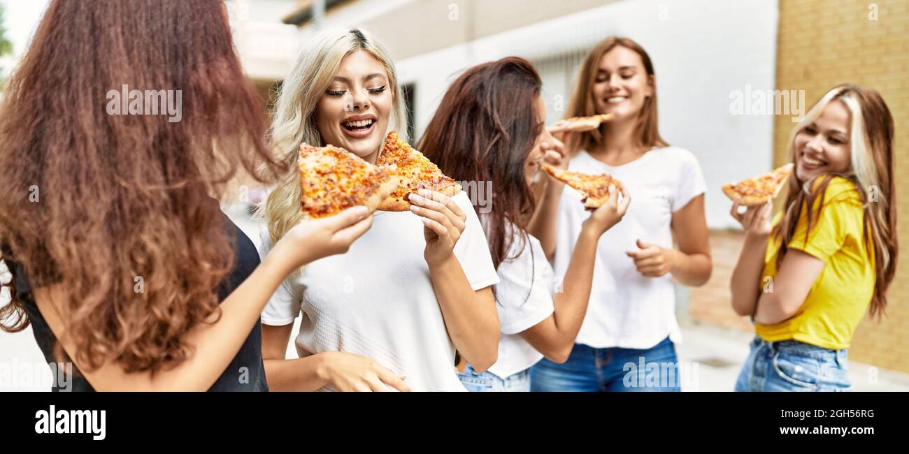 Group of young woman friends smiling happy eating pizza standing at the ...