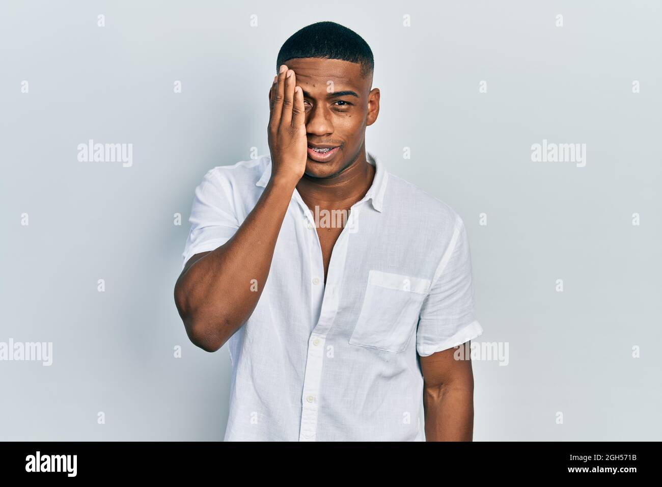 Young black man wearing casual white shirt covering one eye with hand ...