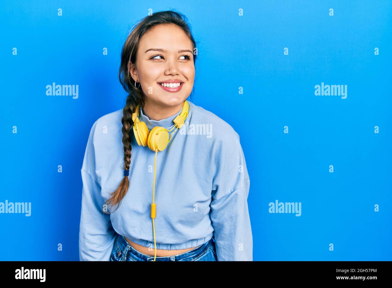 Young hispanic girl listening to music using headphones looking to side ...