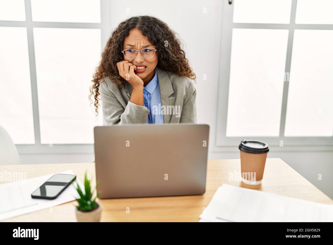 Beautiful hispanic business woman sitting on desk at office working ...