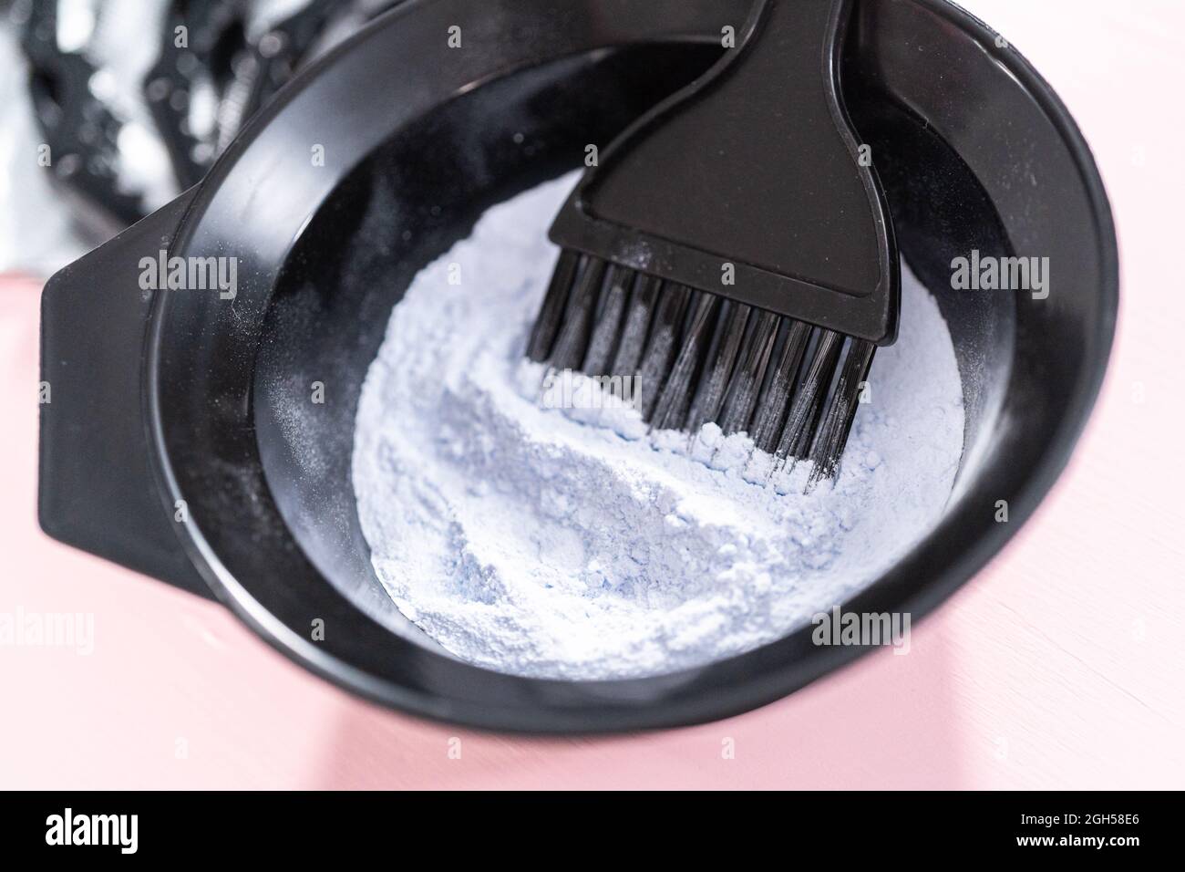 Hair color dye powder in a black plastic mixing bowl on a pink