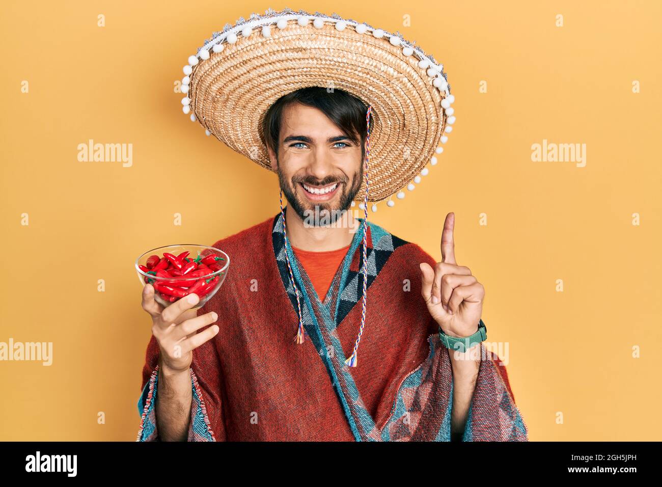 Young hispanic man wearing mexican hat holding chili surprised with an idea or question pointing finger with happy face, number one Stock Photo