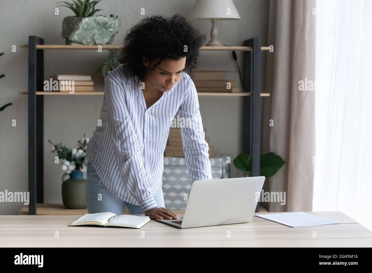Thoughtful black female stand by desk ponder on electronic document Stock Photo