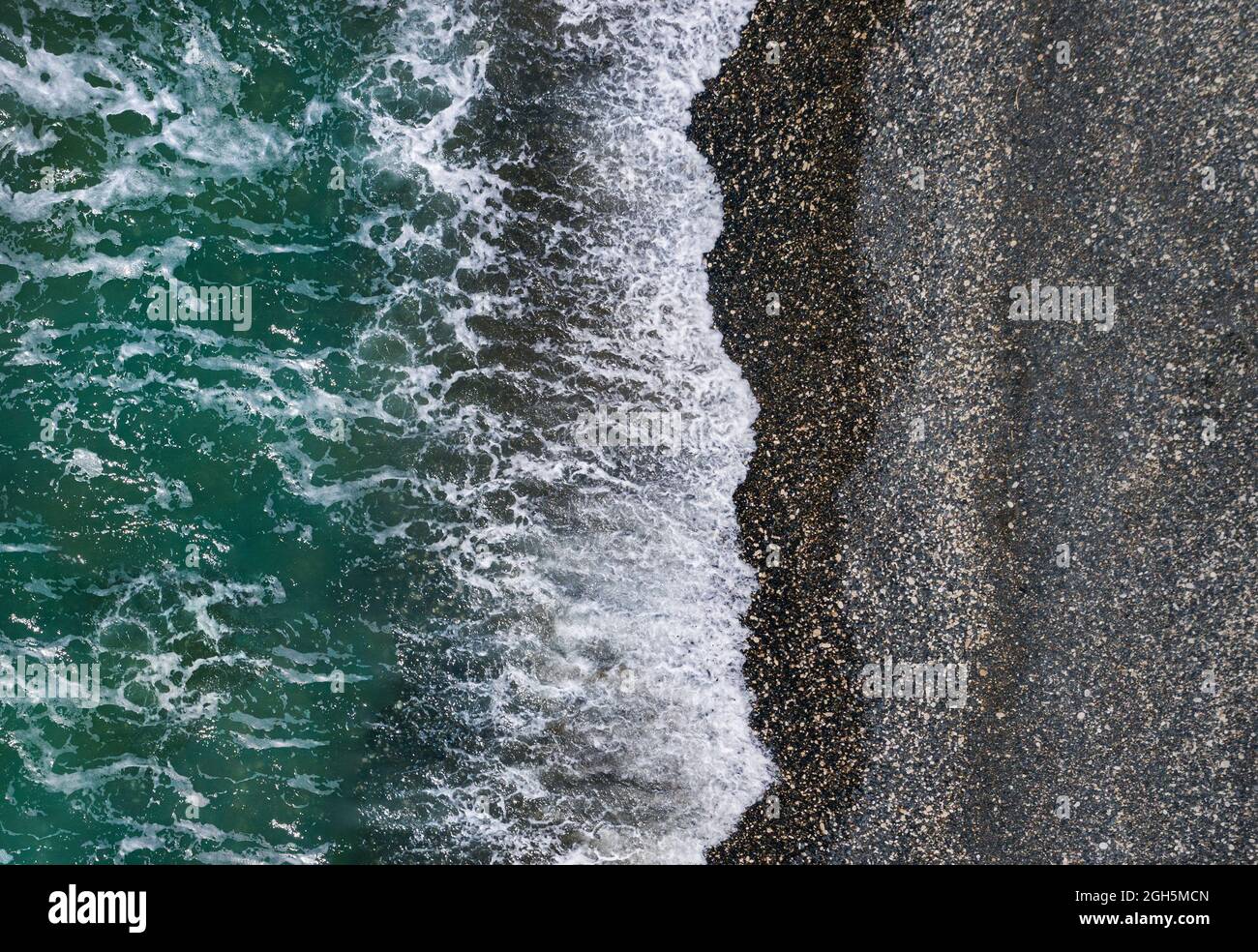 Green sea waves break on black sand and pebbles shore, aerial marine texture Stock Photo