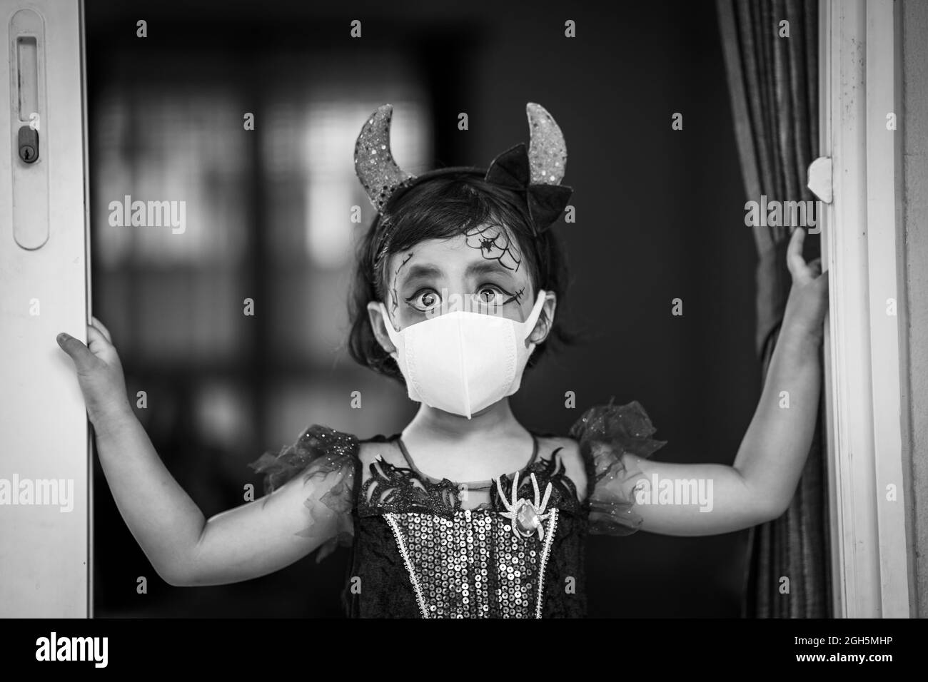 A grayscale shot of a Southeast Asian girl wearing her costume and also a facemask on Halloween Stock Photo