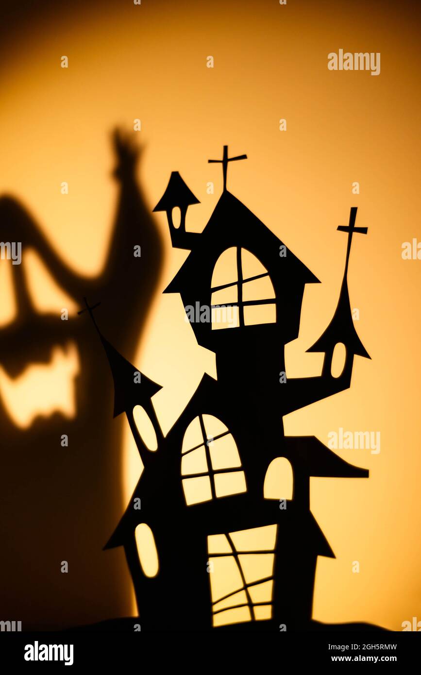 Silhouette of black puppet house casting shadow of ghost on orange wall during Halloween celebration Stock Photo