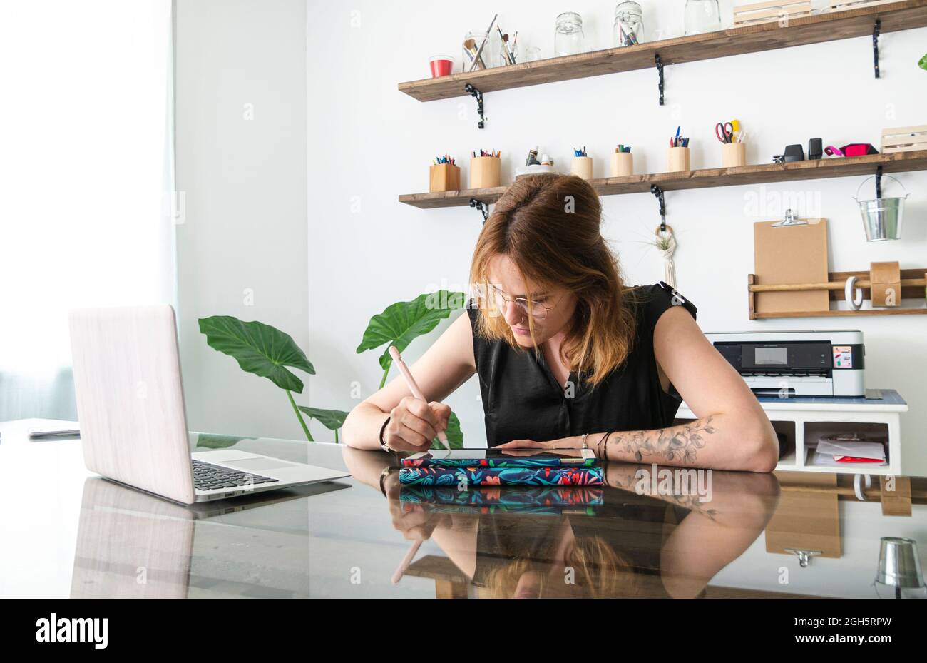 female graphic designer using netbook and tablet with stylus while working on project at table in creative studio Stock Photo