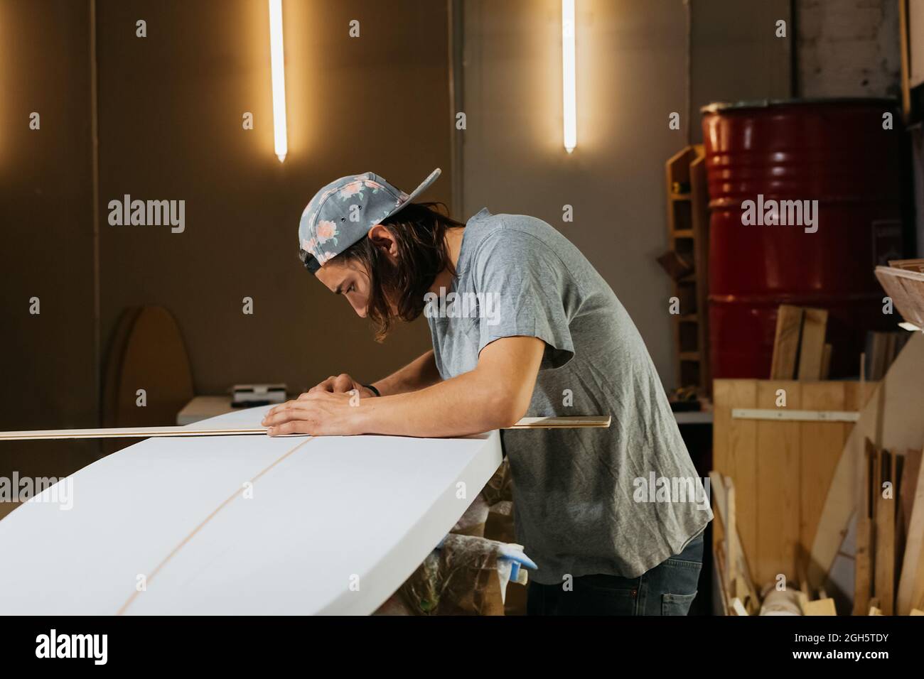 Side view of male shaper using measure tool while working with surfboard in workshop Stock Photo
