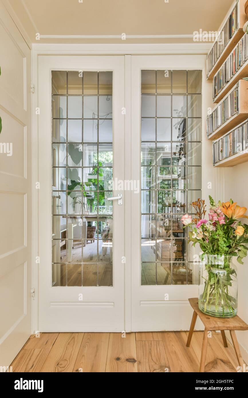 Vase with flowers placed on bench under bookshelves in front of white