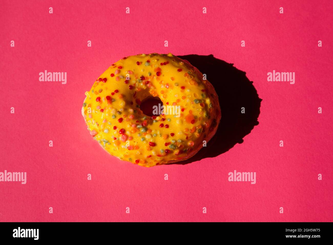 Top view of one donuts coated with a yellow sugar with colored balls on pink background Stock Photo