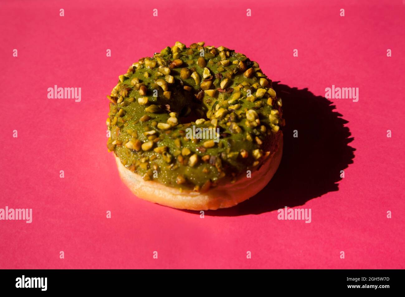 Top view of one donuts coated with a green sugar with nuts on pink background Stock Photo