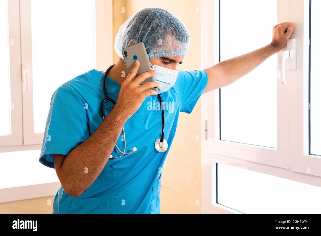 Male medic in uniform and with stethoscope standing in hospital and talking on smartphone Stock Photo