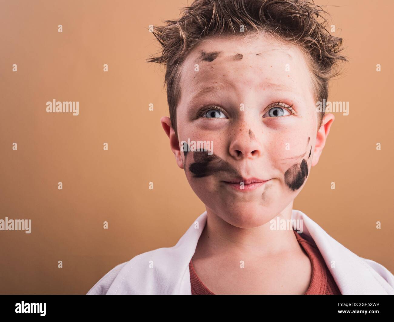 Pondering child with blue eyes and paint blots on face looking up on beige background Stock Photo