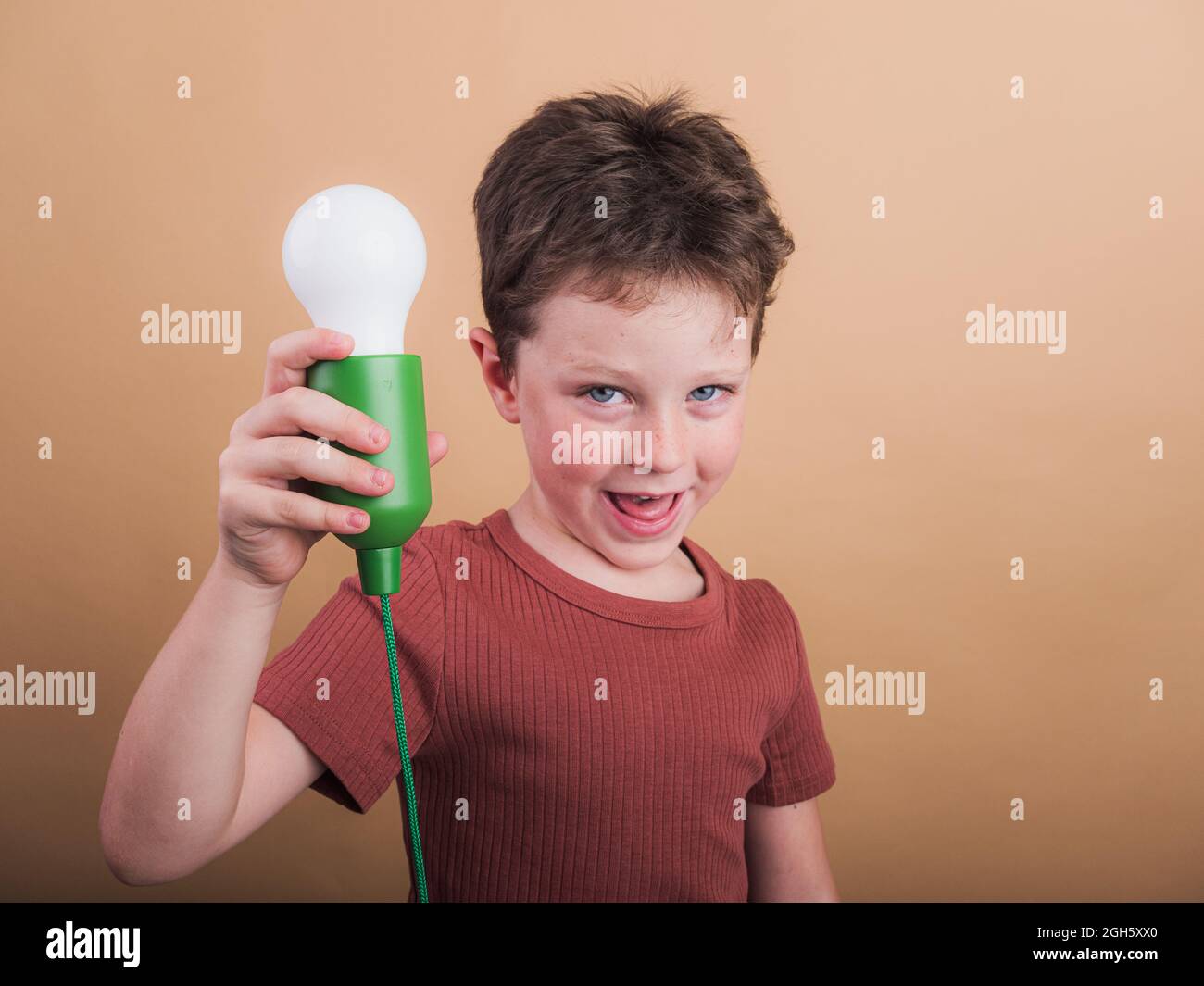 Pondering child in t shirt with plastic light bulb representing idea concept looking at camera on beige background Stock Photo