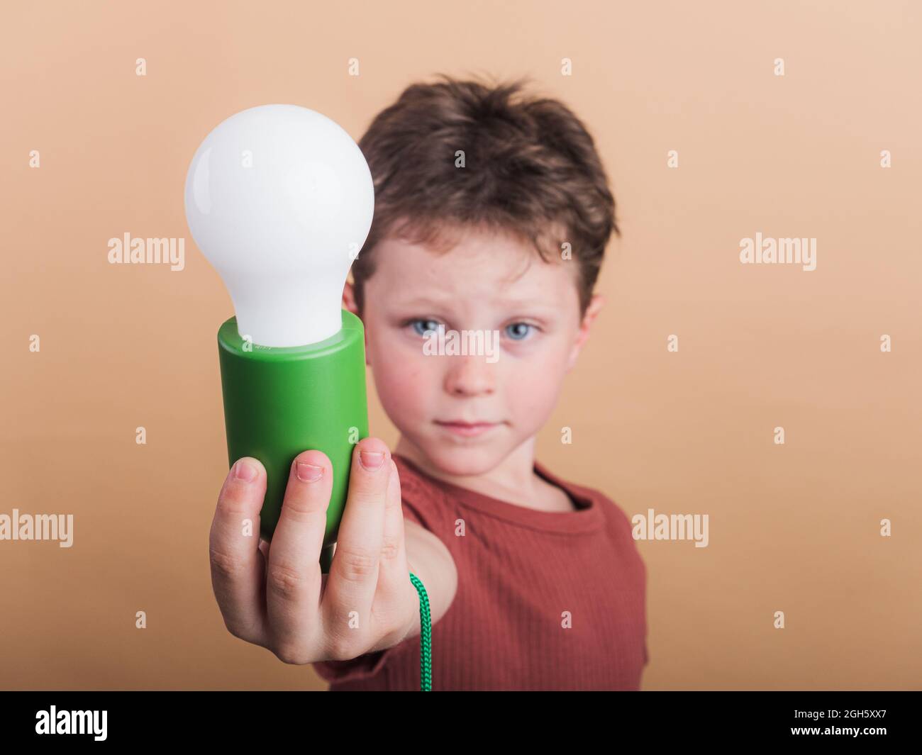 Pondering child in t shirt with plastic light bulb representing idea concept on beige background Stock Photo