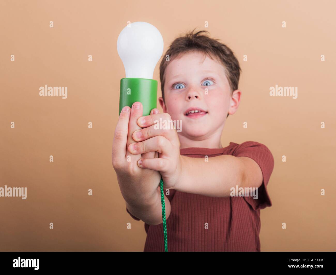 Surprised child in t shirt with plastic light bulb representing idea concept on beige background Stock Photo