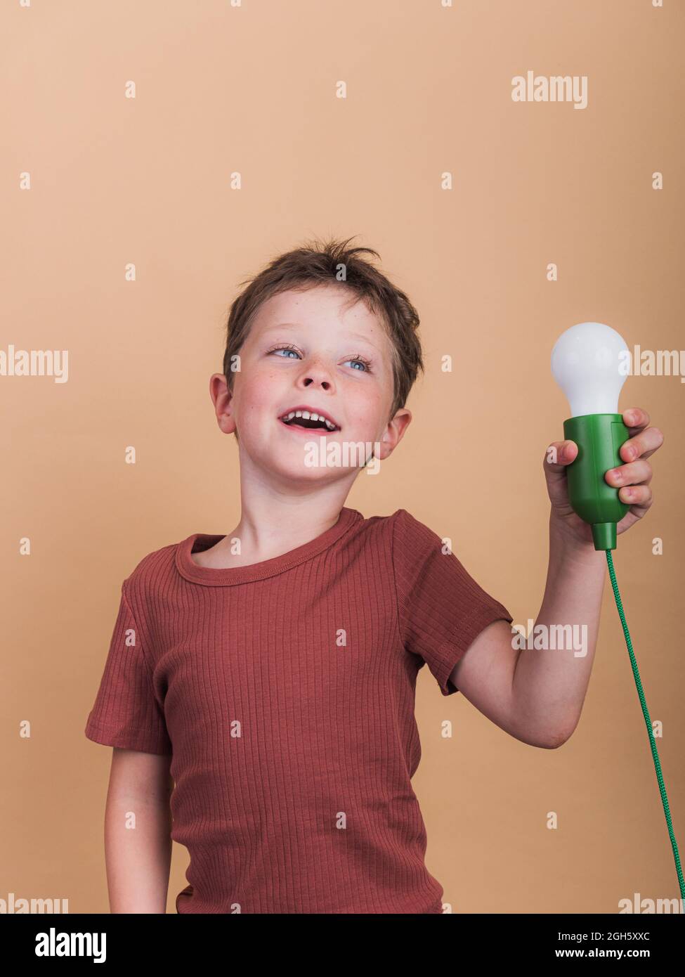 Pondering child in t shirt with plastic light bulb representing idea concept looking up on beige background Stock Photo