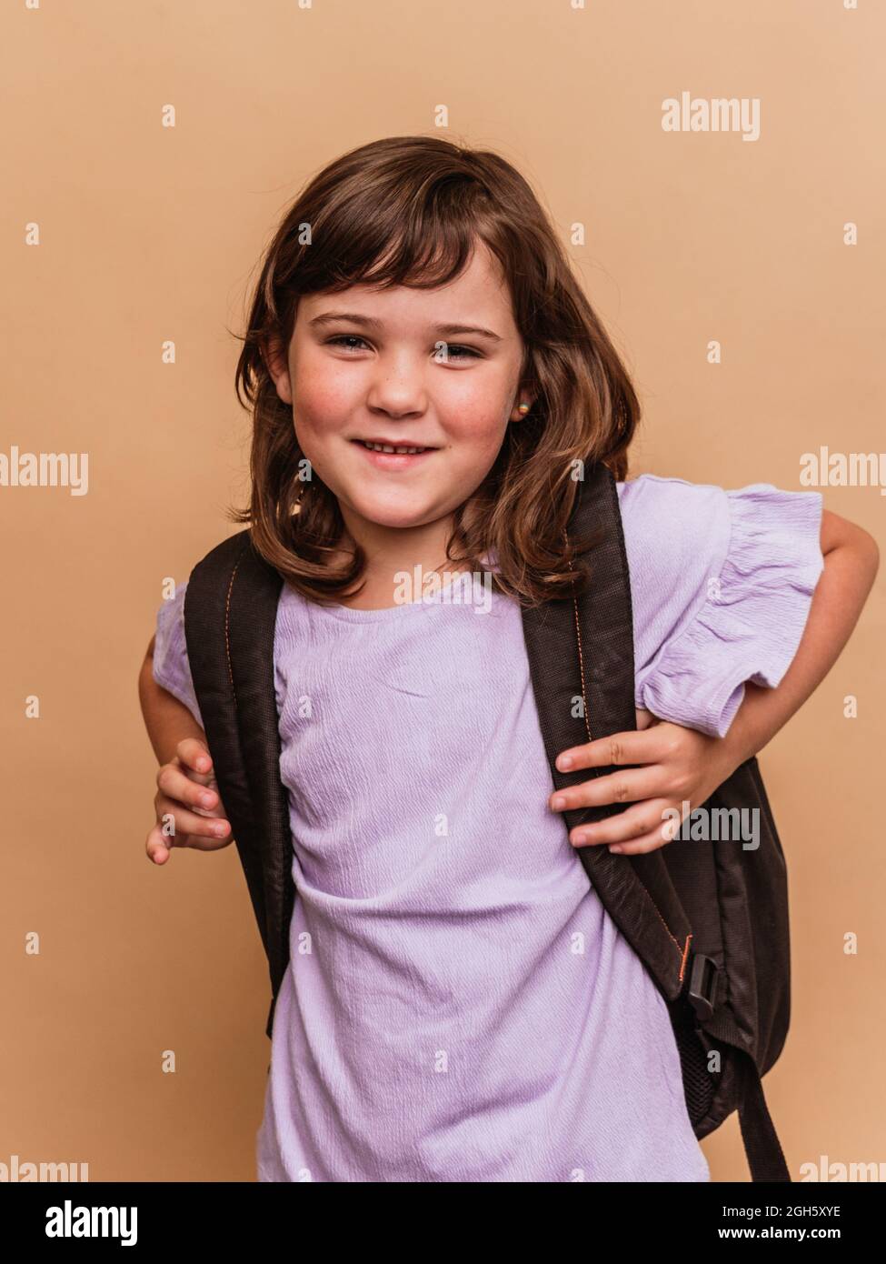 Cute schoolchild standing on brown background in studio and looking at camera Stock Photo