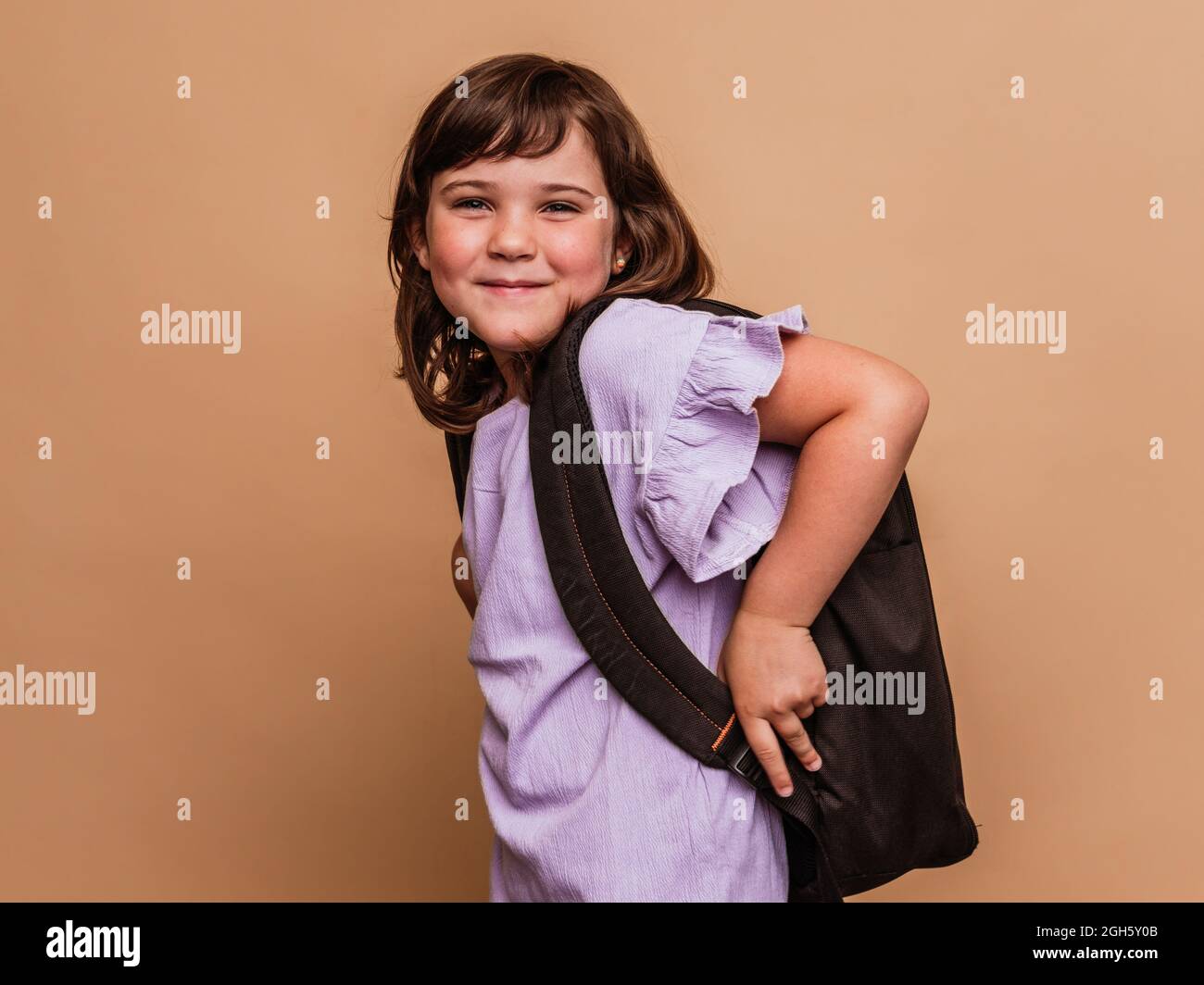 Cute schoolchild standing on brown background in studio and looking at camera Stock Photo