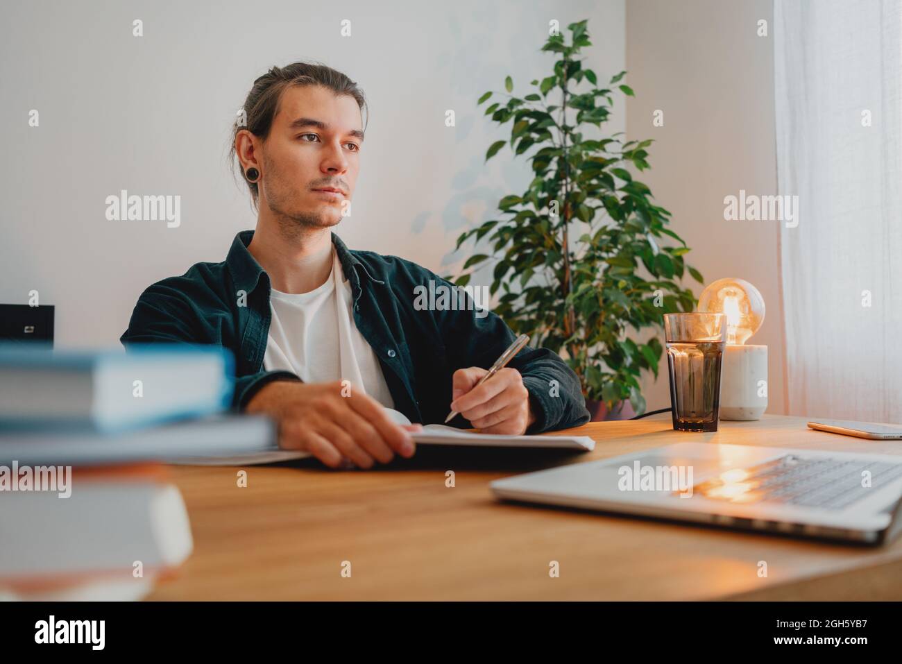 College student preparing for pass exam at home. Young man making notes while online learning Stock Photo