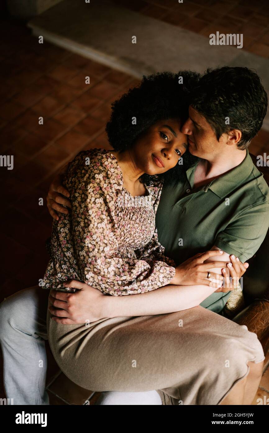 From above of loving black Woman sitting on knees of man while embracing at home Stock Photo photo