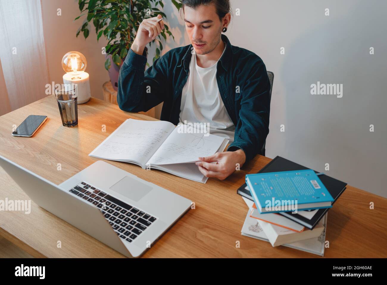 College student preparing for pass exam at home. Young man making notes while online learning Stock Photo