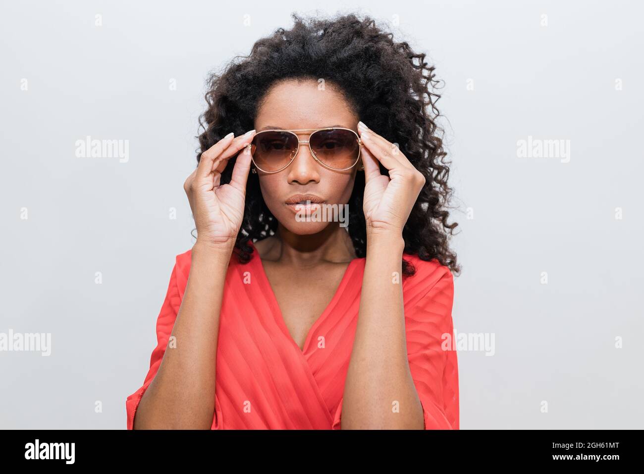 Trendy young African American female with curly hair in red wear and sunglasses looking at camera Stock Photo