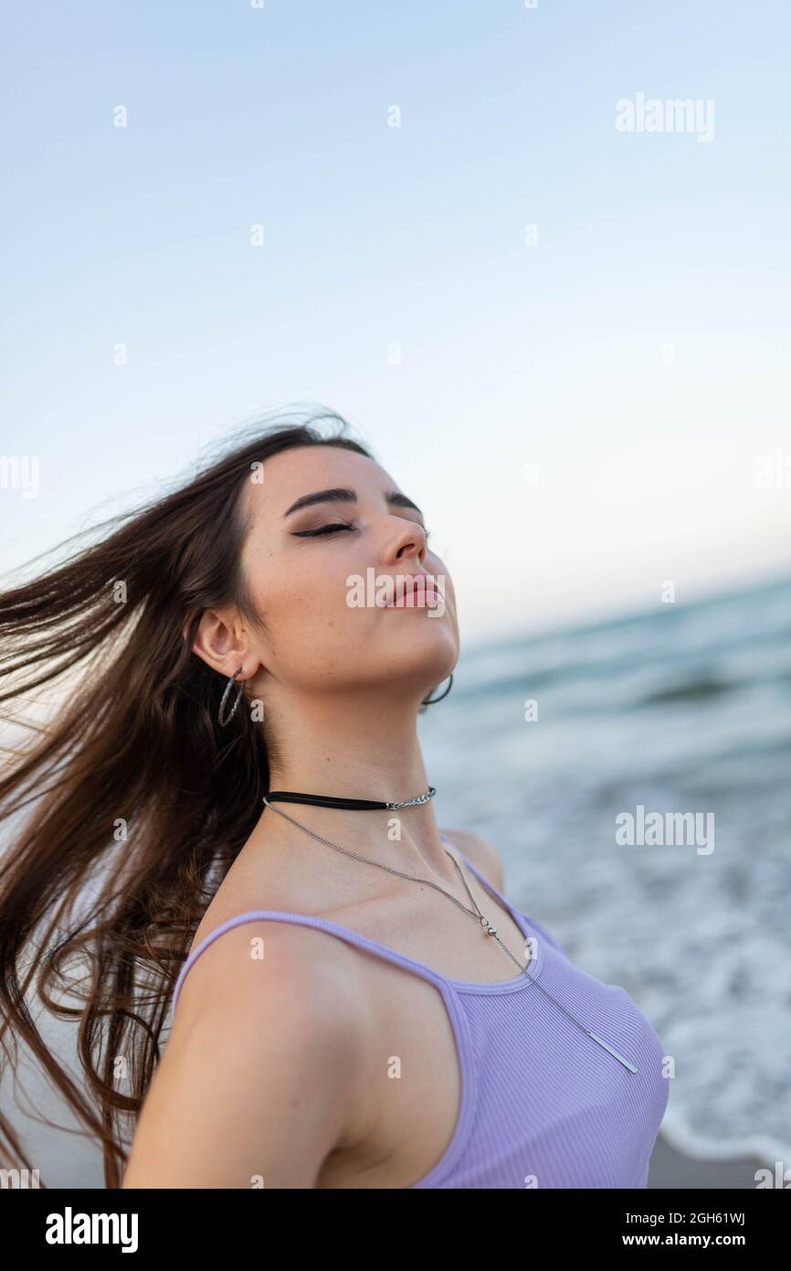 Young with closed eyes shaking long hair against sea and