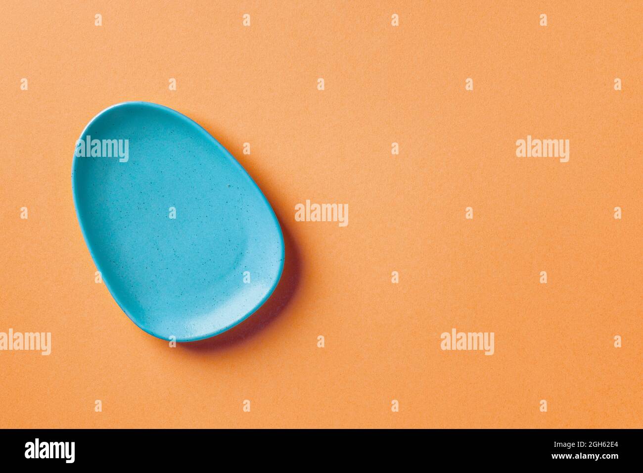 Blue ceramic oval plate on an orange background. Modern ceramic crockery, serveware and dinnerware. Blank dinner plate for trendy color food design. Stock Photo