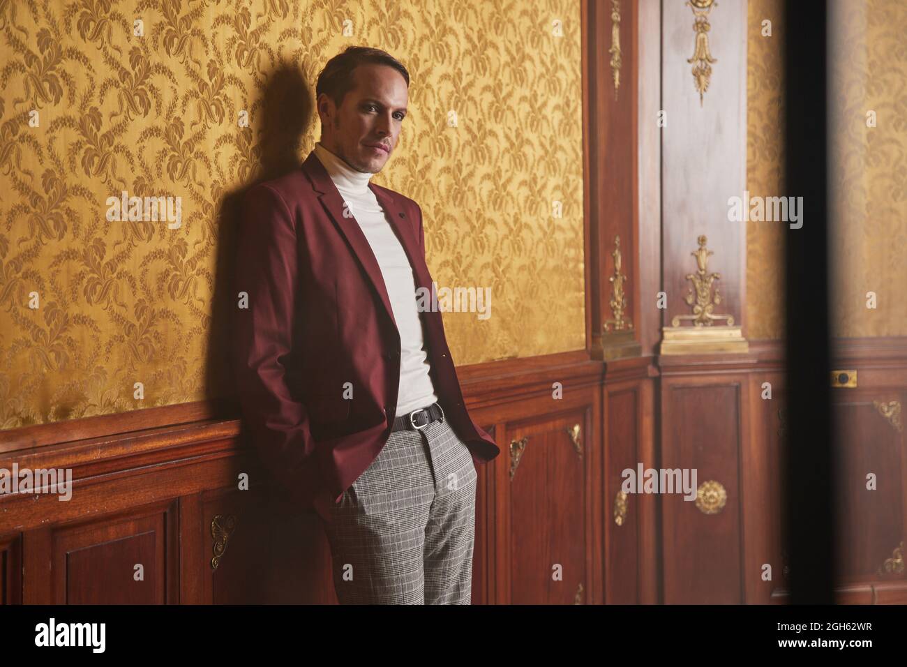 Confident adult male actor in elegant classy clothes keeping hand in pocket and looking away thoughtfully while standing near wall in vintage style ro Stock Photo