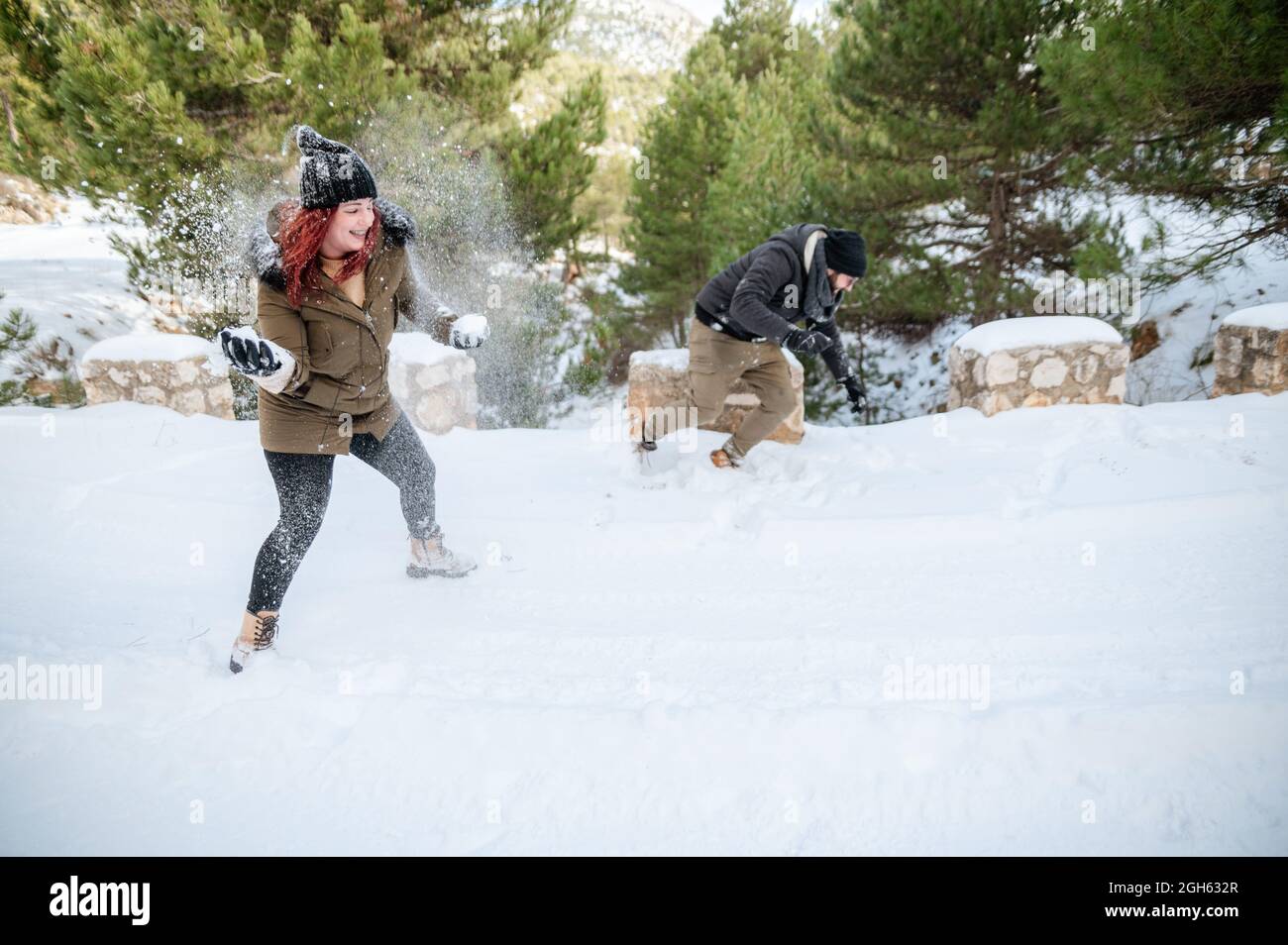 Cheerful friends in warm clothes playing snowballs in forest while enjoying winter day and having fun Stock Photo