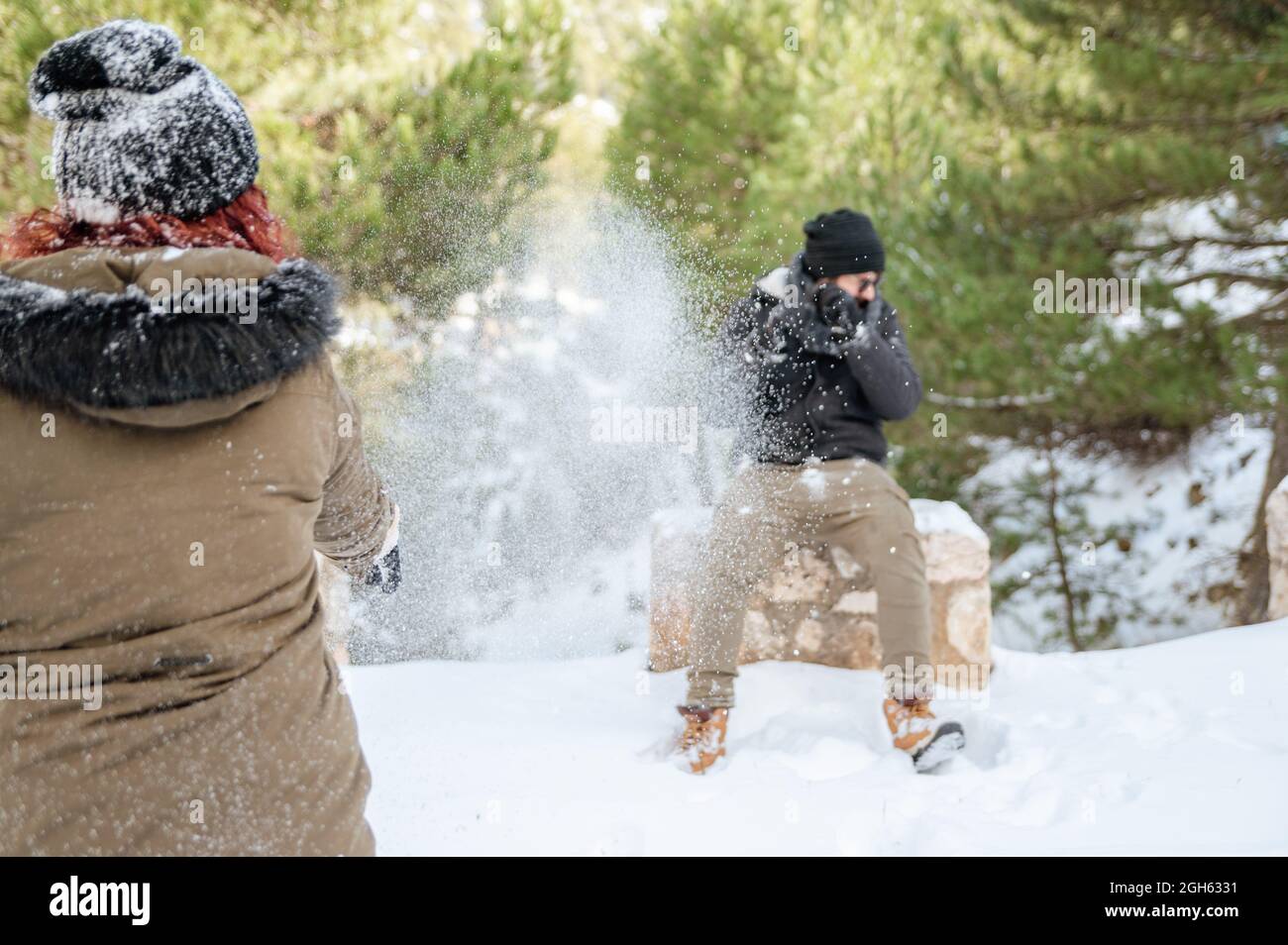 Cheerful friends in warm clothes playing snowballs in forest while enjoying winter day and having fun Stock Photo