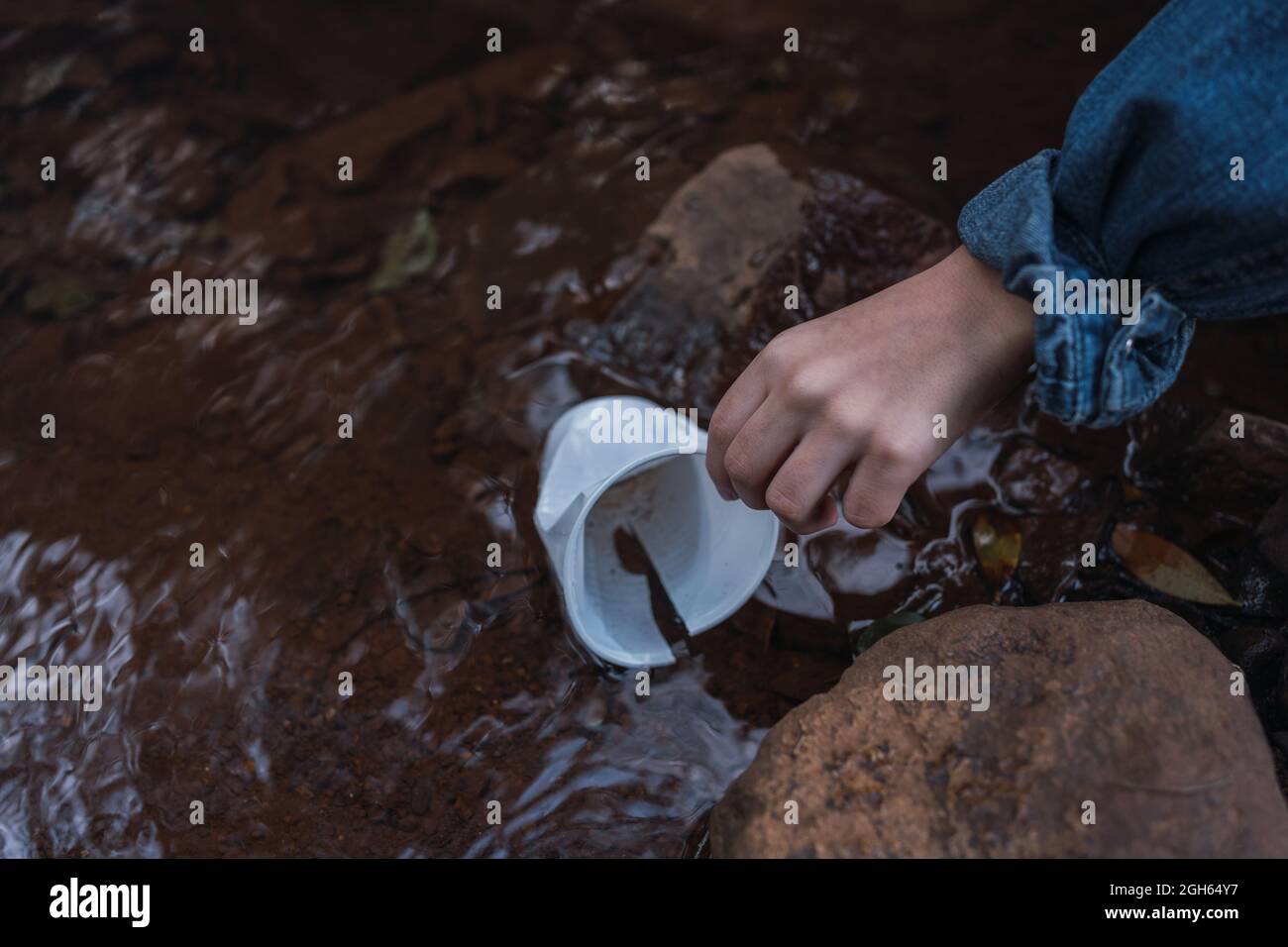 From above of crop anonymous person picking up disposable glass from shallow river with stones in daytime Stock Photo