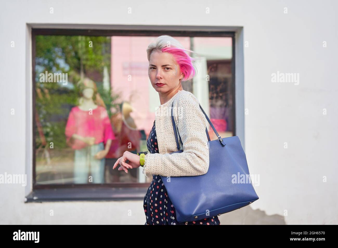 Side view of trendy informal female with dyed hair walking on street and looking at camera Stock Photo