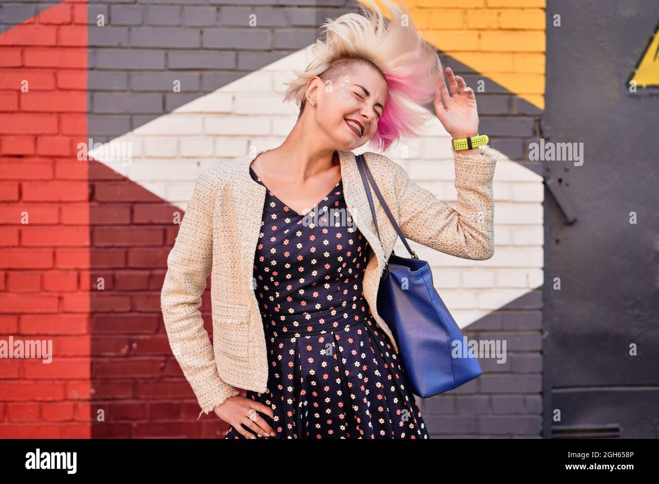 Carefree alternative female throwing dyed short hair against colorful wall in urban area Stock Photo