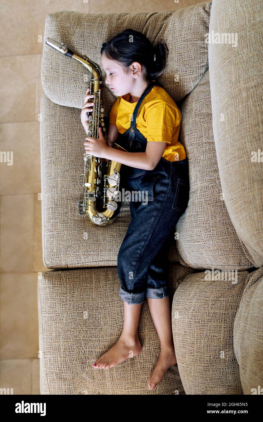 From above side view of barefoot child with saxophone napping on couch in house room Stock Photo