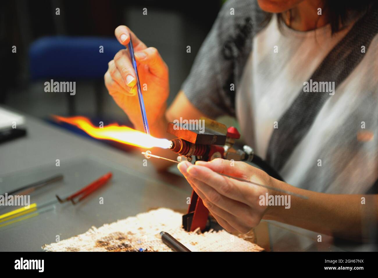 work of a glassblower. Women's hands hold the burner and melt the glass. Soft selective focus, noise. Stock Photo
