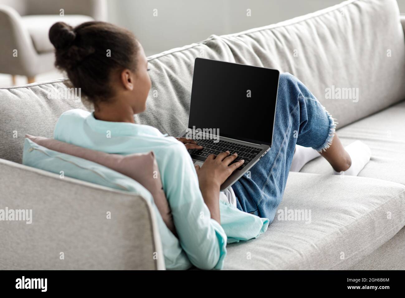 Teen african american girl typing on laptop with empty screen and study at home interior Stock Photo