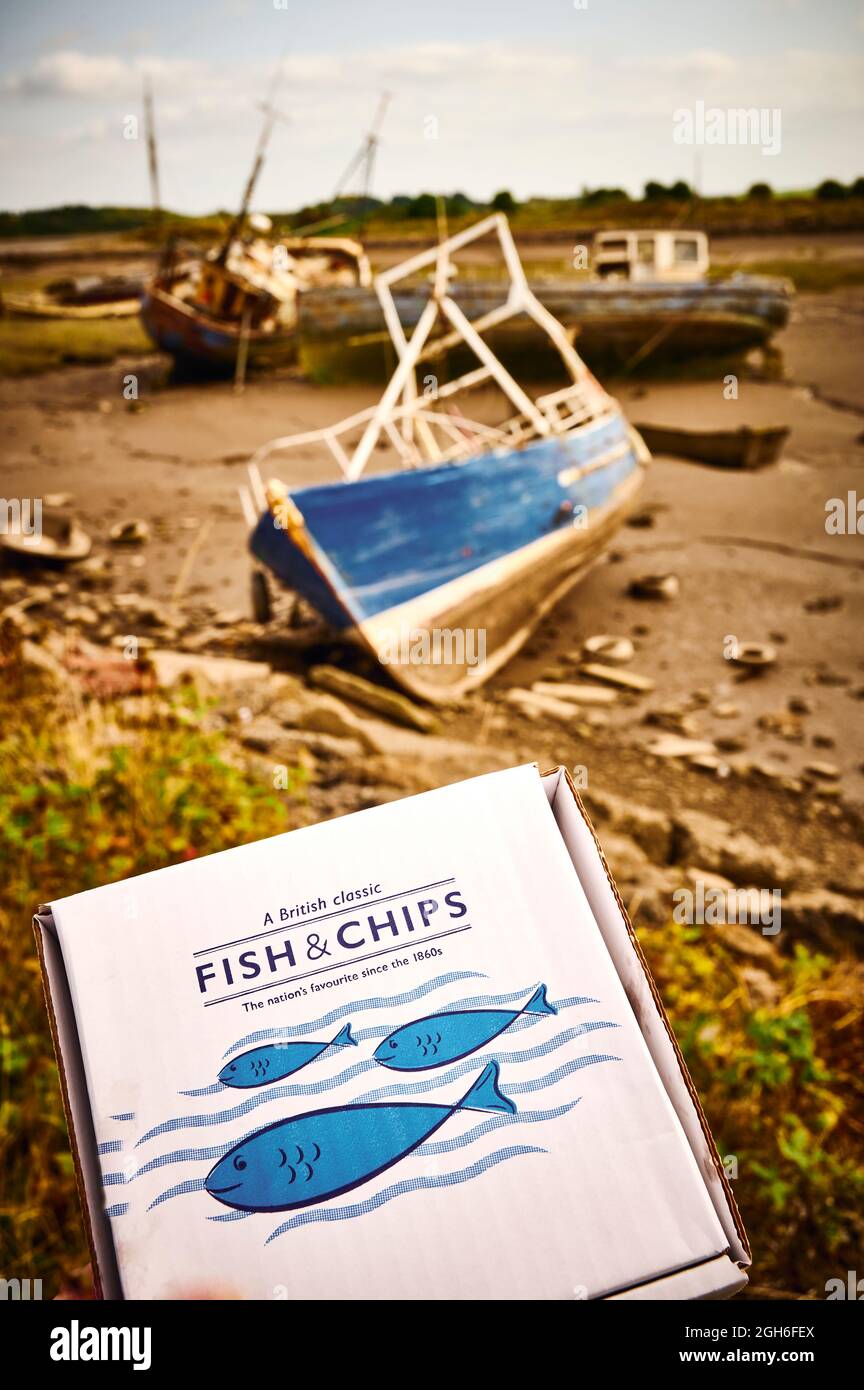 A cardboard box containing fish and chips held in front of abandoned