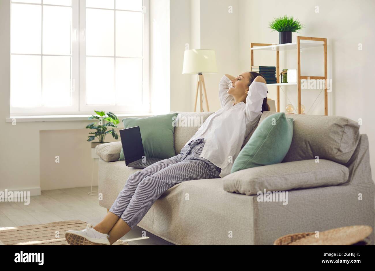 Woman sitting on sofa with hands behind head, relaxing, feeling happy and satisfied Stock Photo